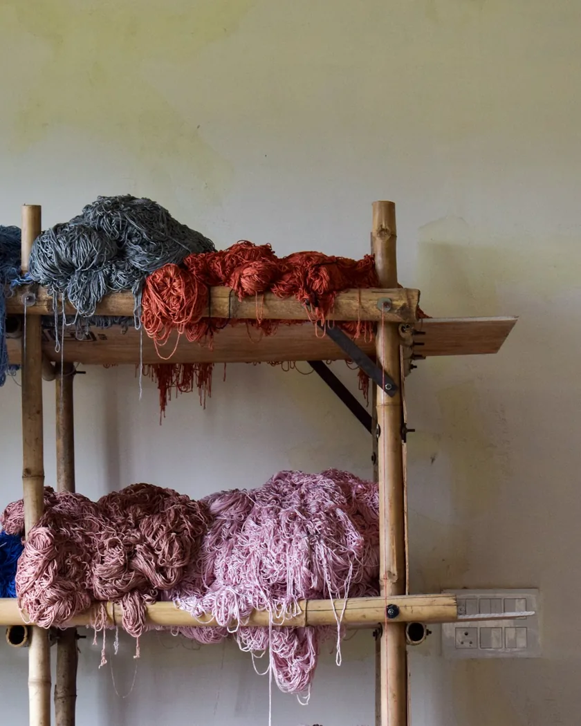 Madejas de hilo de distintos colores y grosores ordenadas en un estante de madera del taller